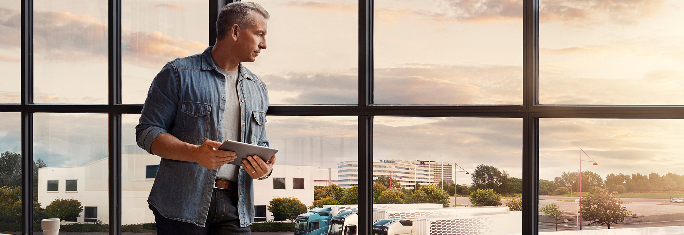 Een man met een tablet staat bij een raam en kijkt neer over zijn wagenpark