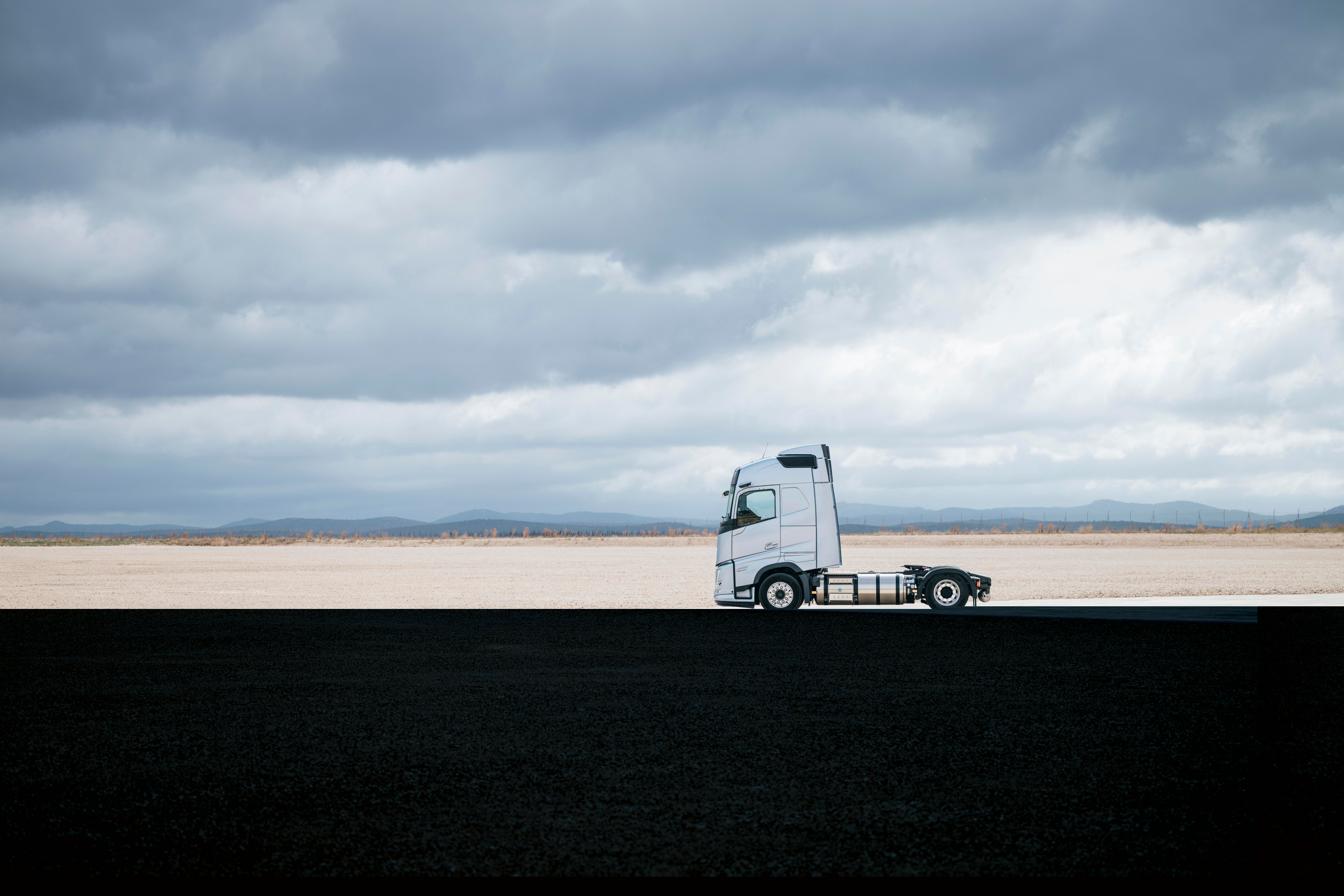 Zijaanzicht van een Volvo-vrachtwagen geparkeerd op een breed, open landschap onder een bewolkte hemel, met een weidse omgeving en minimale bezienswaardigheden.